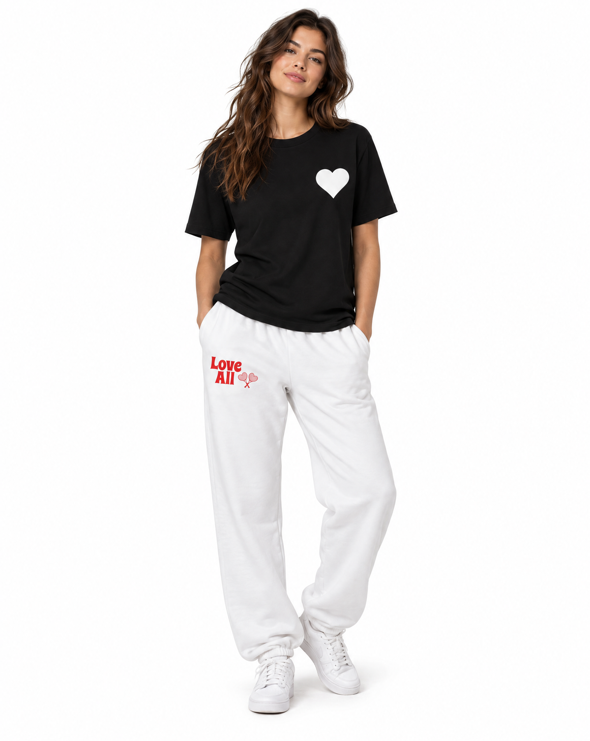 A woman modeling a black short-sleeve t-shirt with a white heart on the chest and white sweatpants with red 'Love All' text and a heart graphic on the left thigh, paired with white sneakers, against a plain white background.