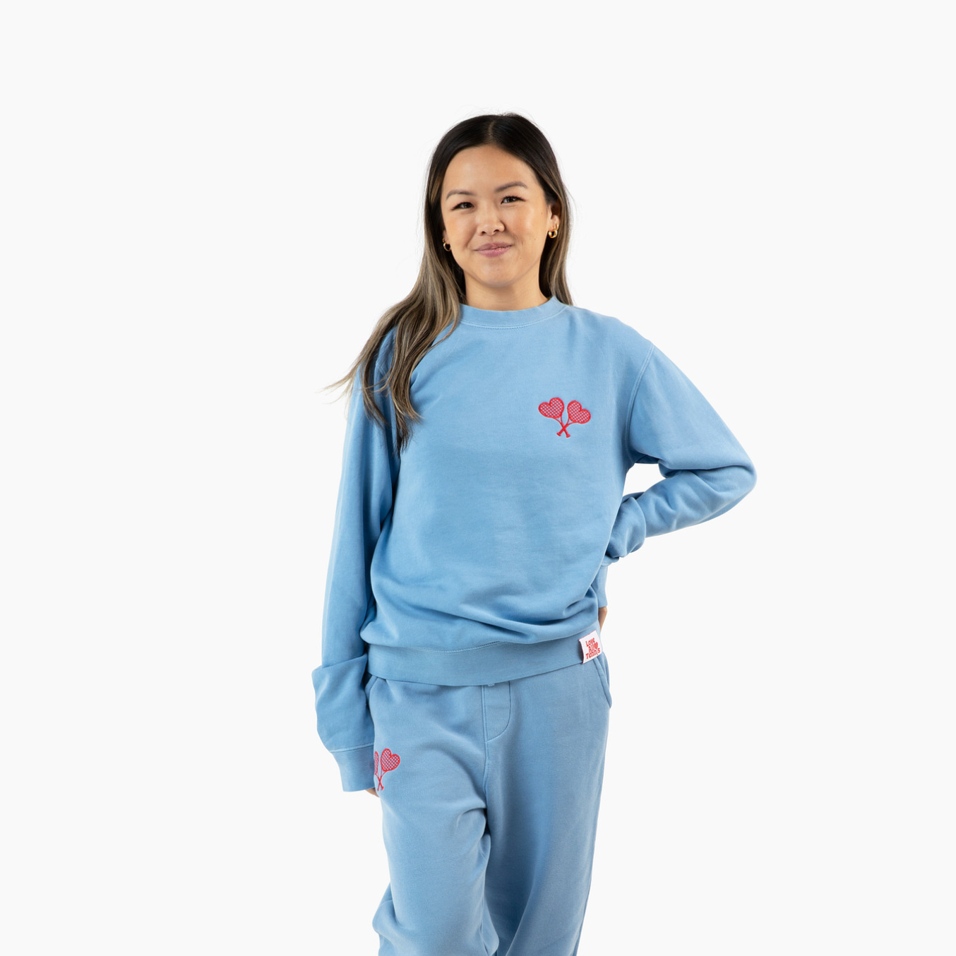 Person wearing a light blue sweatshirt and pants with a red logo on a white background