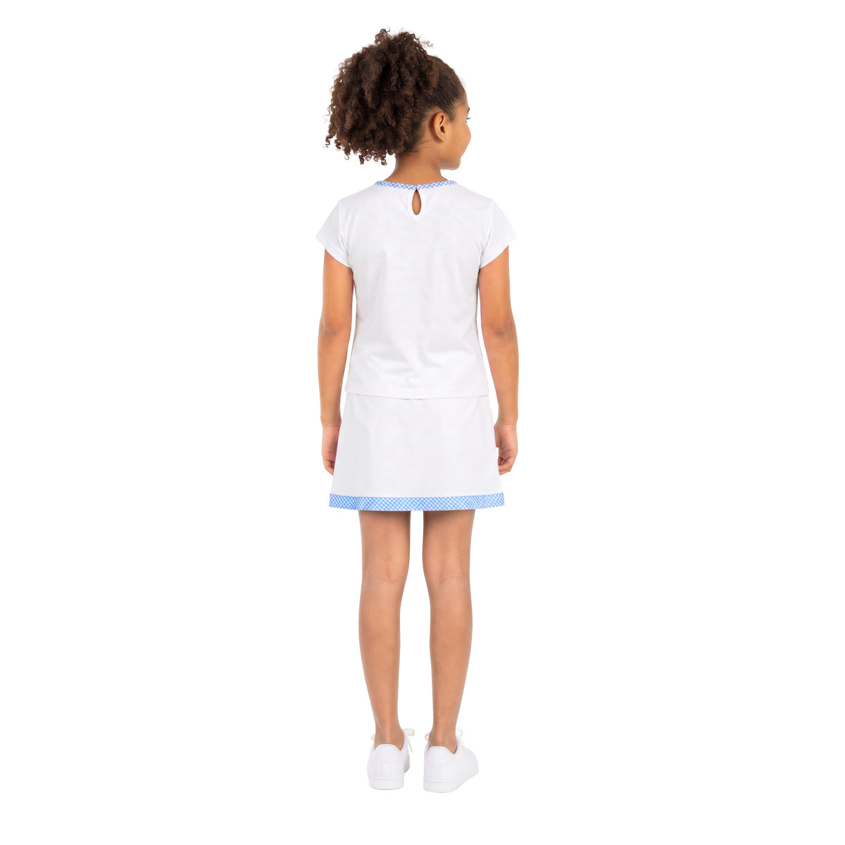 A young girl viewed from behind wearing a white short-sleeve top and skirt with light blue trim at the collar and hem, paired with white sneakers, on a solid white background.