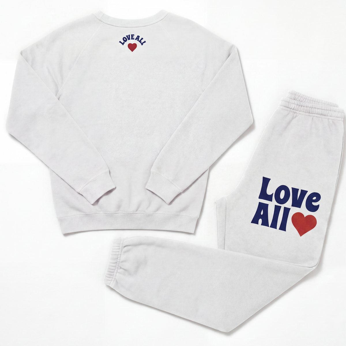 A matching white sweatshirt and sweatpants set laid flat on a white background. The sweatshirt has 'LOVE ALL' printed in navy blue with a red heart on the upper back.