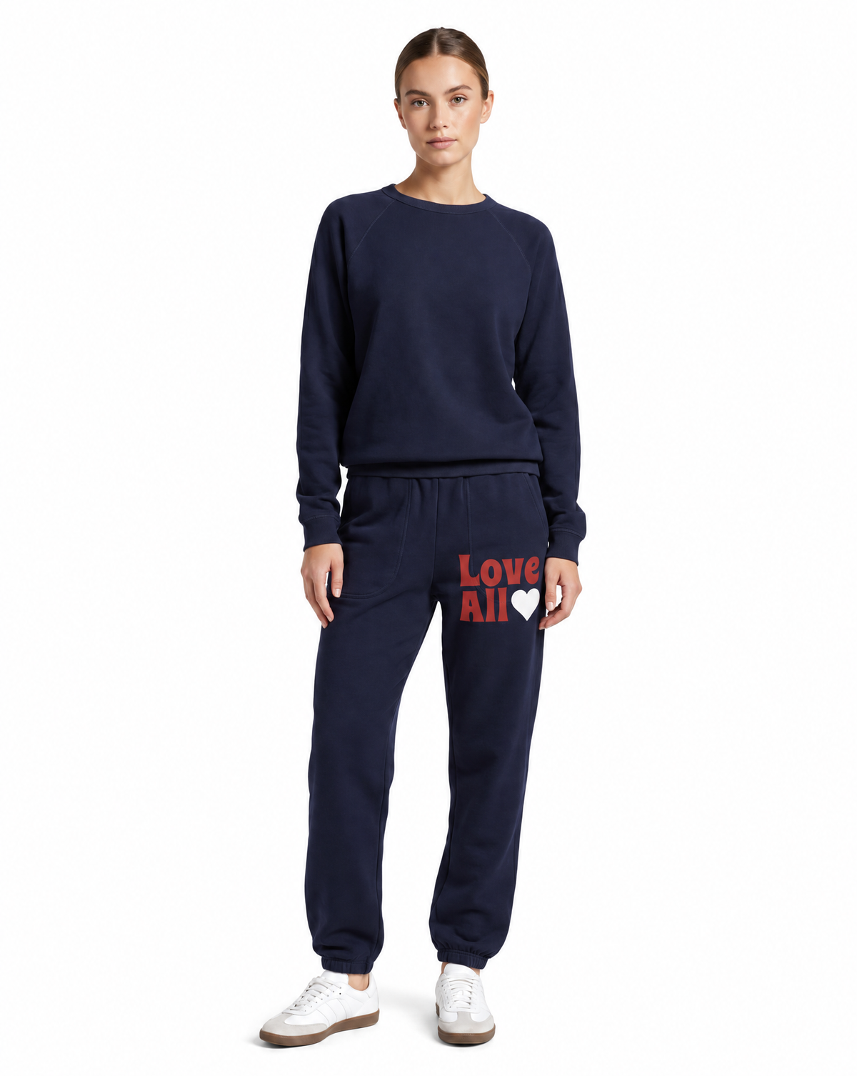 A woman modeling a navy blue sweatshirt and matching jogger pants set. The jogger pants feature the text 'Love All' in red and a white heart on the left thigh.
