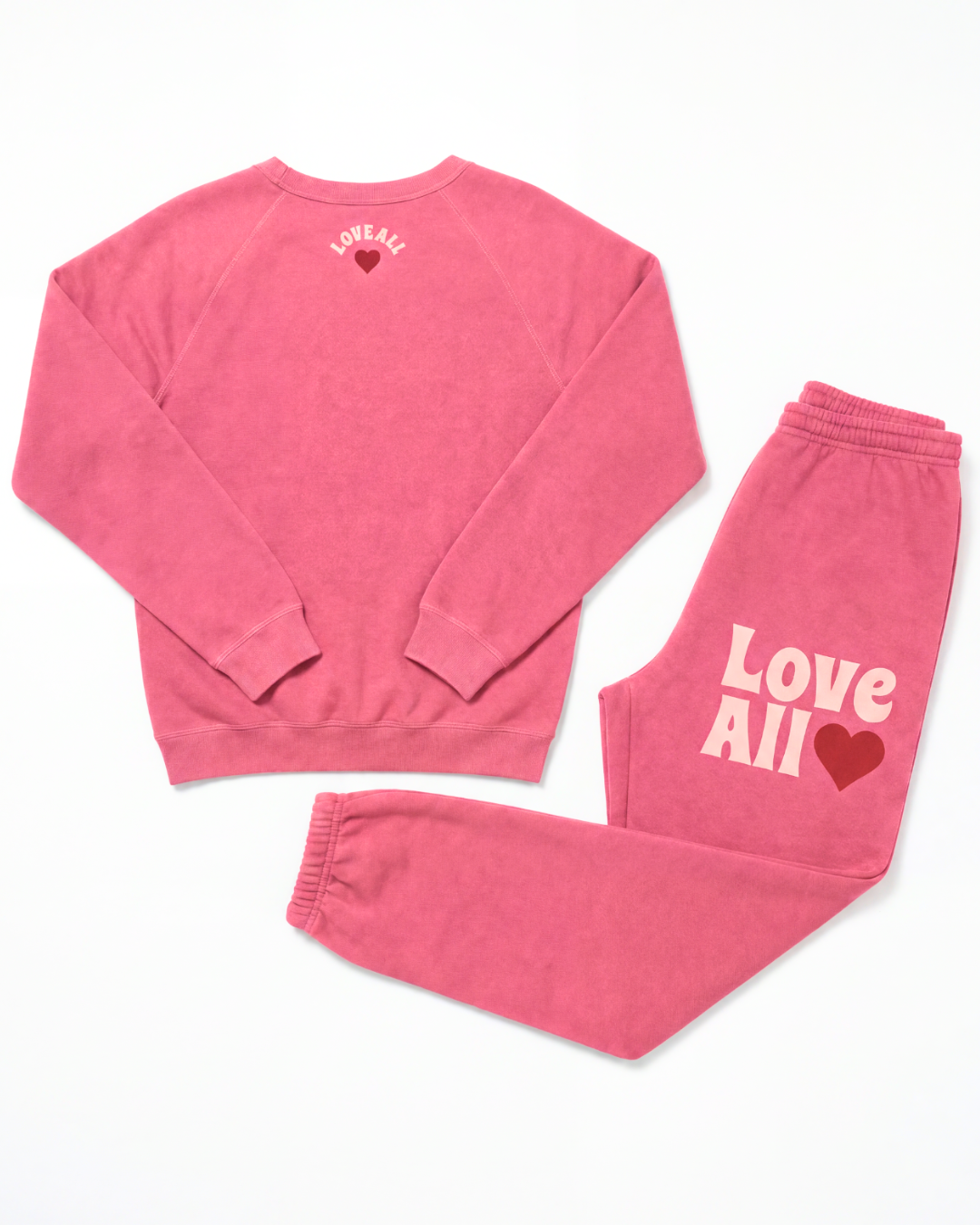 A two-piece loungewear set in a washed pink color, featuring a long-sleeve crewneck sweatshirt and matching jogger pants. The sweatshirt has a small 'Love All' heart graphic on the back, and the pants feature a larger 'Love All' text and heart graphic on