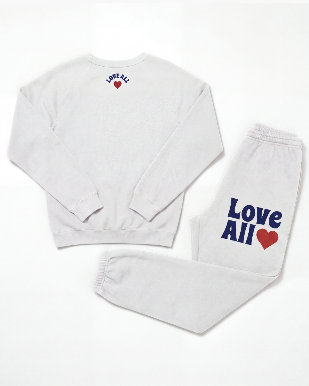 A white sweatshirt and matching sweatpants set laid flat on a white background. The sweatshirt has 'LOVE ALL' printed in blue with a small red heart on the upper back.