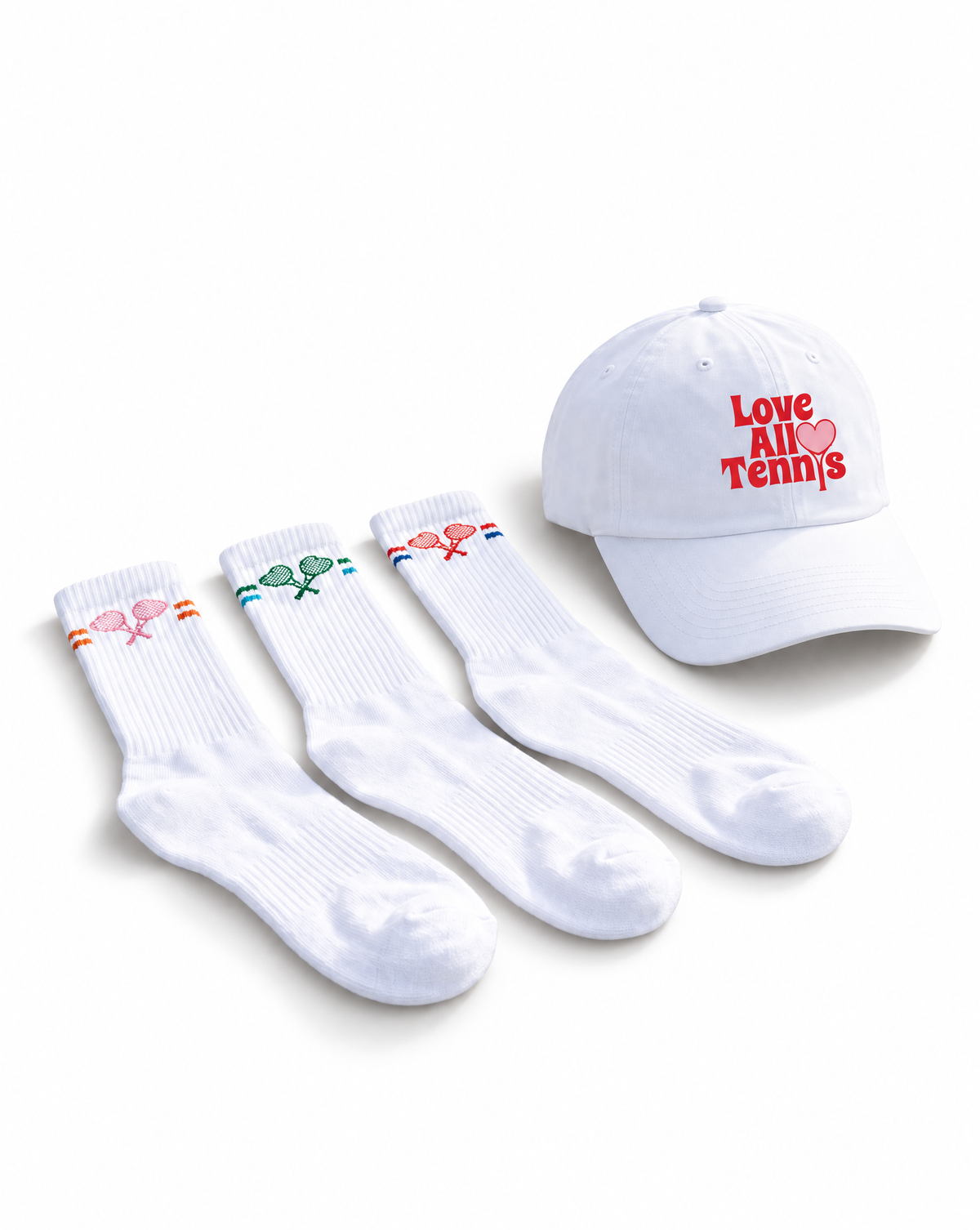A white baseball cap and three white crew socks arranged on a white background. The cap has red embroidered text reading 'Love All Tennis' with a small red heart, and each sock has a small tennis-themed accent in orange, green, or red near the cuff.
