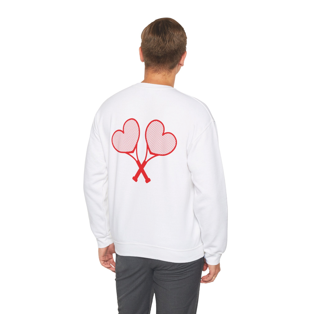 Man showing off the back of a white sweatshirt with red heart tennis rackets that are crossed and grey pants set against a white background