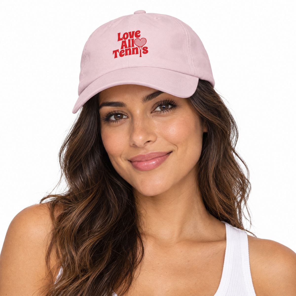 A woman wearing a light pink baseball cap with red embroidered text reading 'Love All Tennis' and a small red heart, shown against a plain white background.