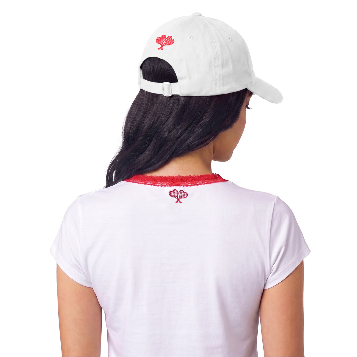A woman shown from the back wearing a white baseball cap and a white short-sleeve T-shirt, both featuring a small red graphic centered below the collar. The background is solid white.