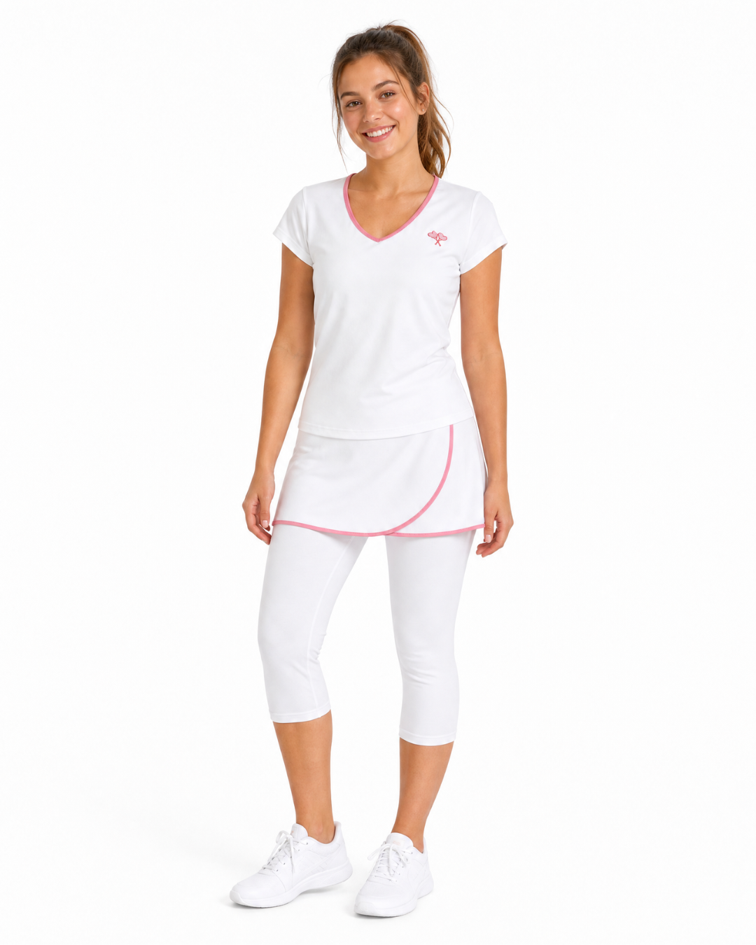 A woman modeling a white athletic set with pink trim, consisting of a V-neck short-sleeve top, a matching mini skirt, and capri leggings, against a plain white background.