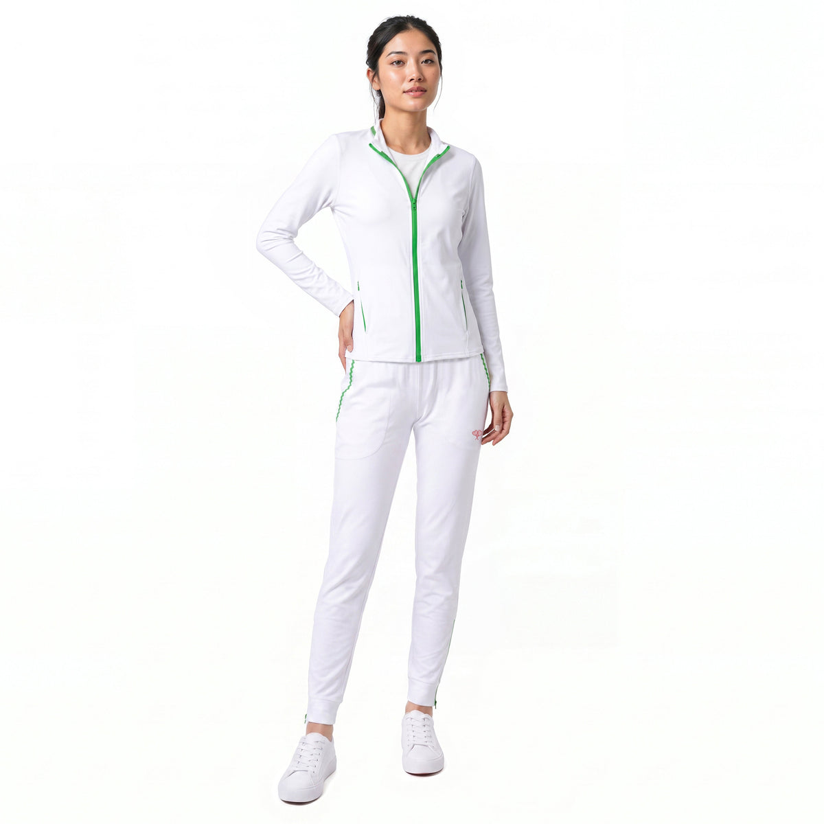 A woman modeling a white athletic tracksuit with bright green zipper and piping details, paired with white sneakers, against a solid white background.