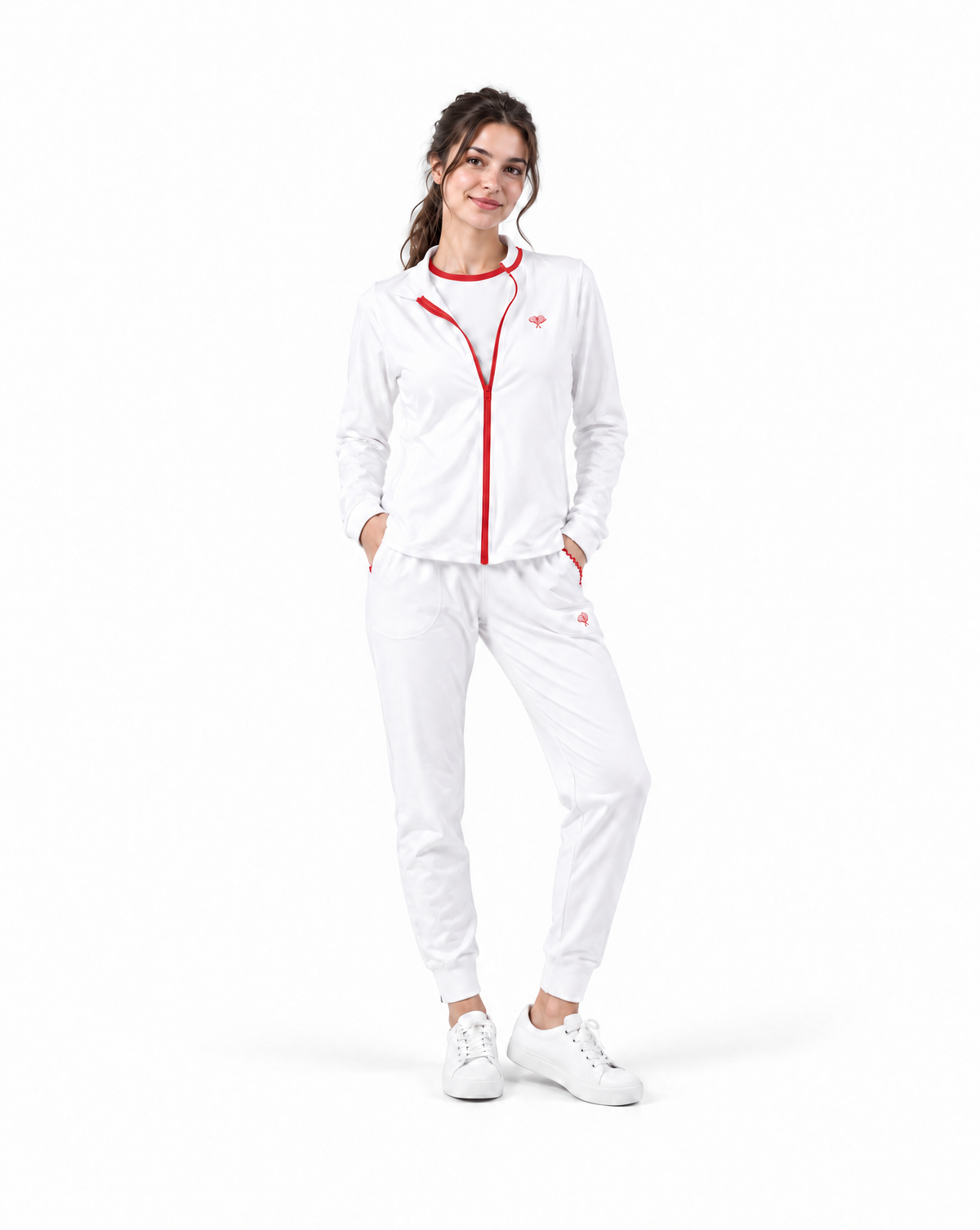 A woman modeling a white athletic tracksuit with red trim and a red front zipper, paired with white sneakers, on a solid white background.