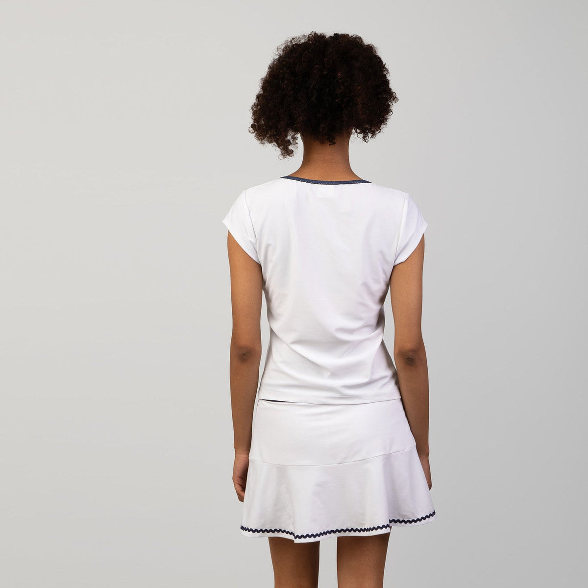 Person wearing a white tennis skort and top with a skirt on a plain background