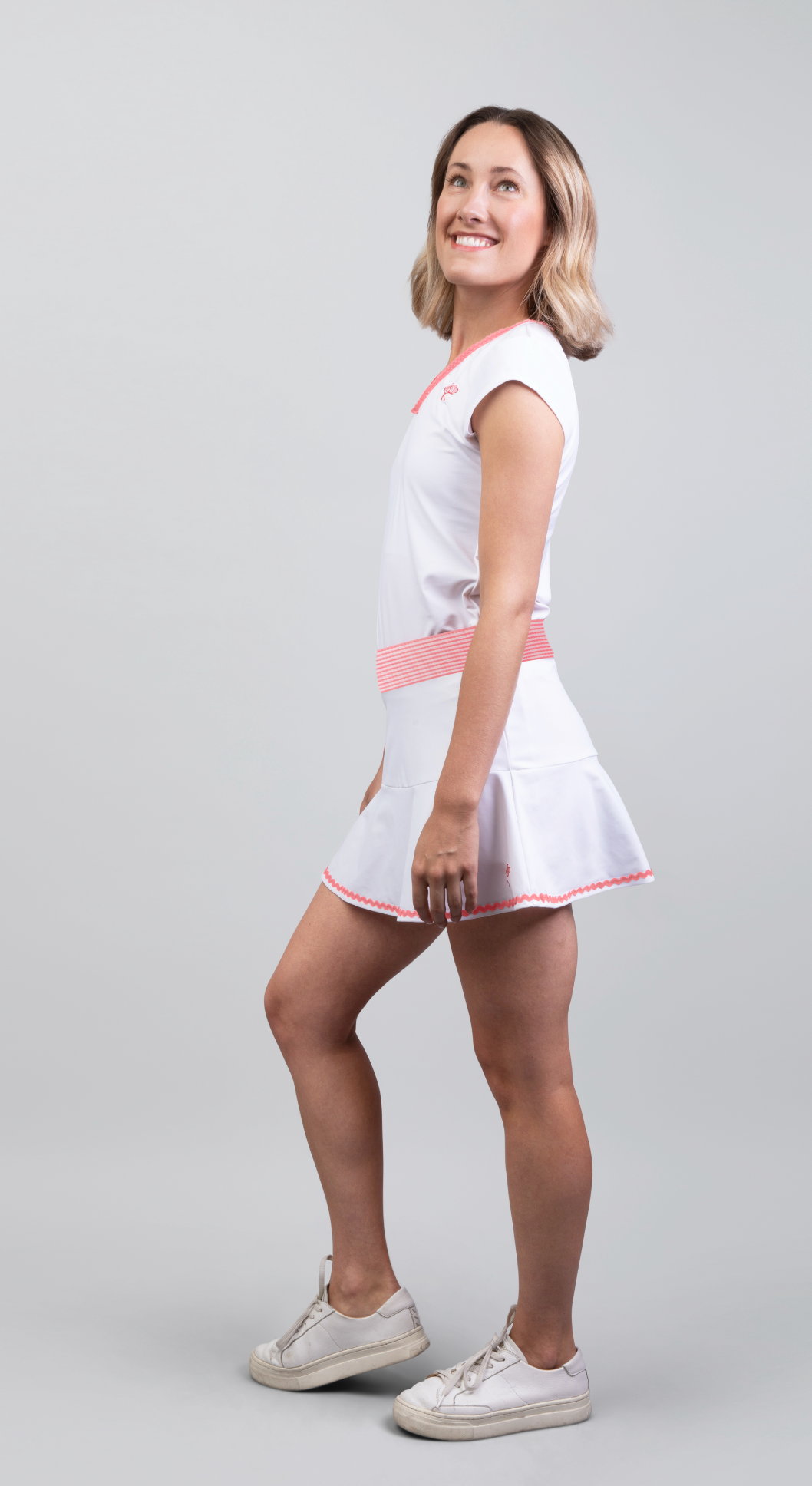 Woman wearing a white dress with pink accents on a gray background