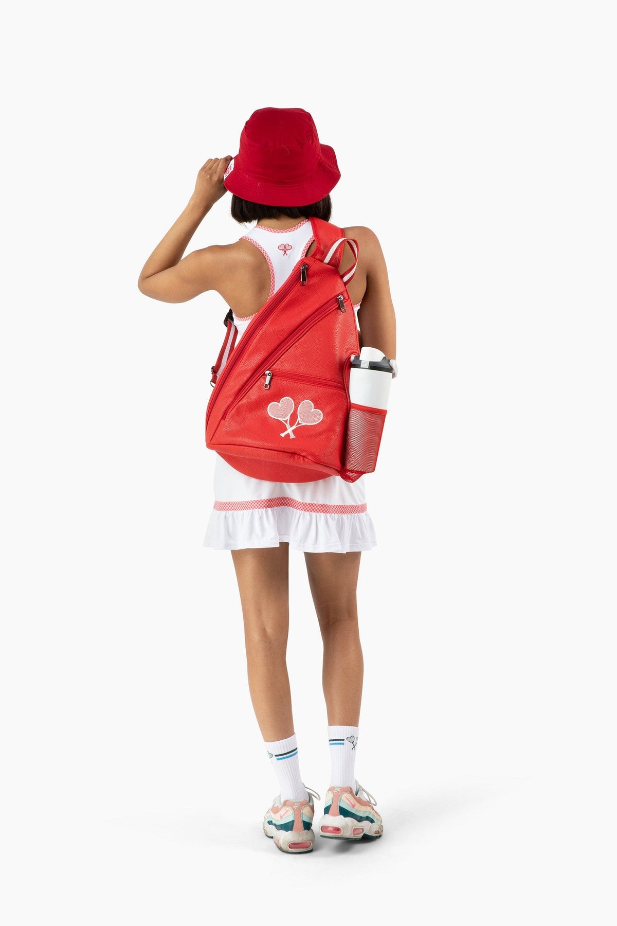 Woman wearing tennis outfit and backpack with red bucket hat and sneakers on set against a white background