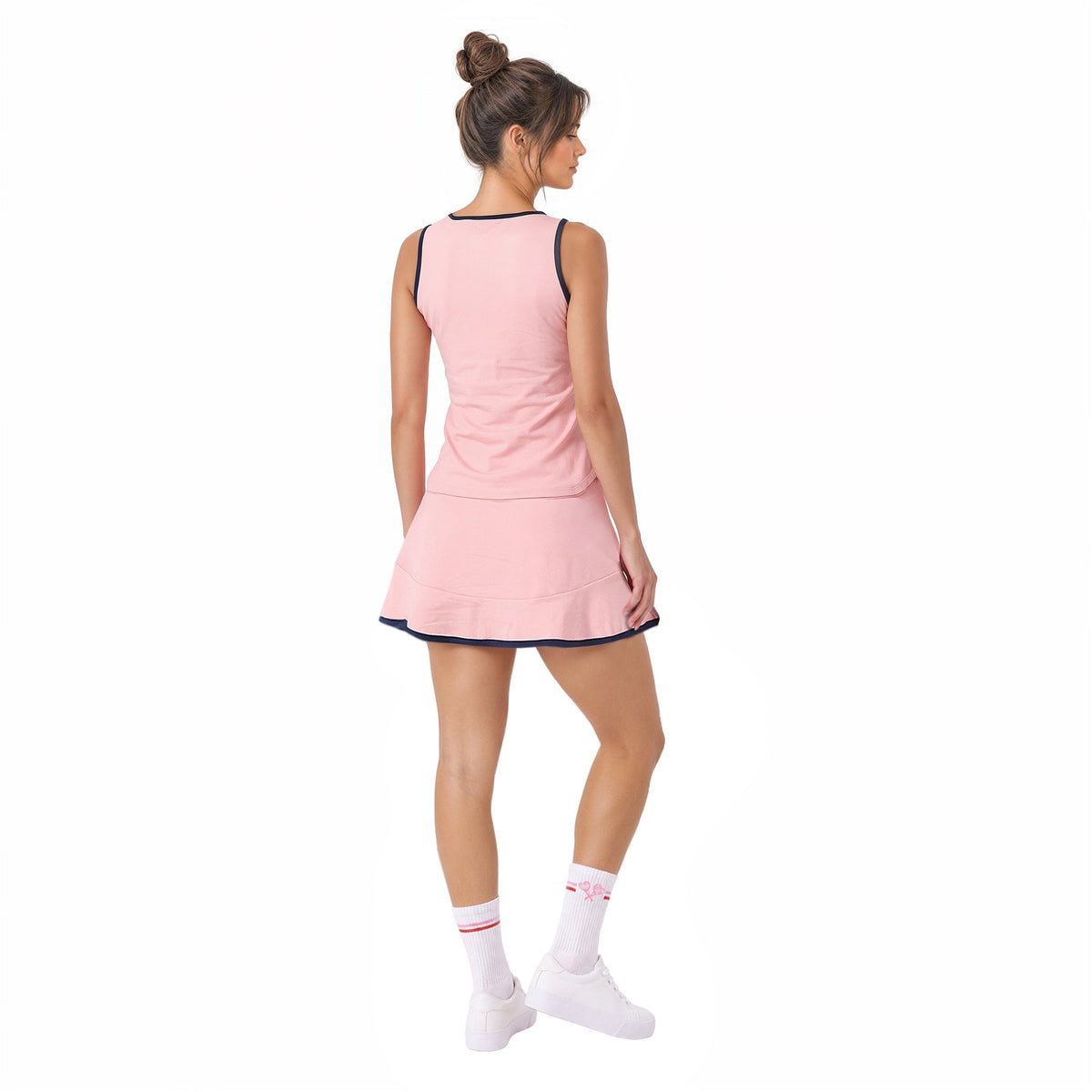 A woman modeling a light pink sleeveless tennis dress with dark navy trim, shown from a rear three-quarter view against a plain white background.