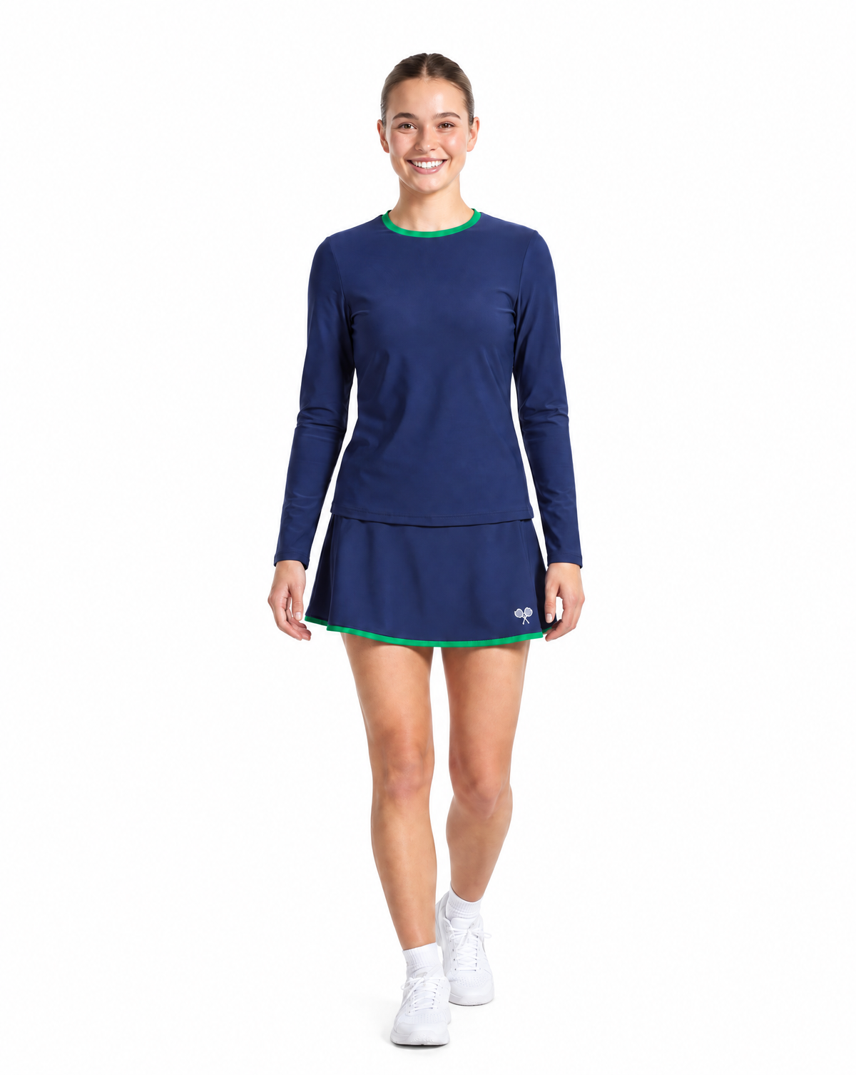 A woman wearing a navy blue long-sleeve athletic dress with a flared skirt and thin green trim, paired with white socks and white sneakers, on a plain white background.