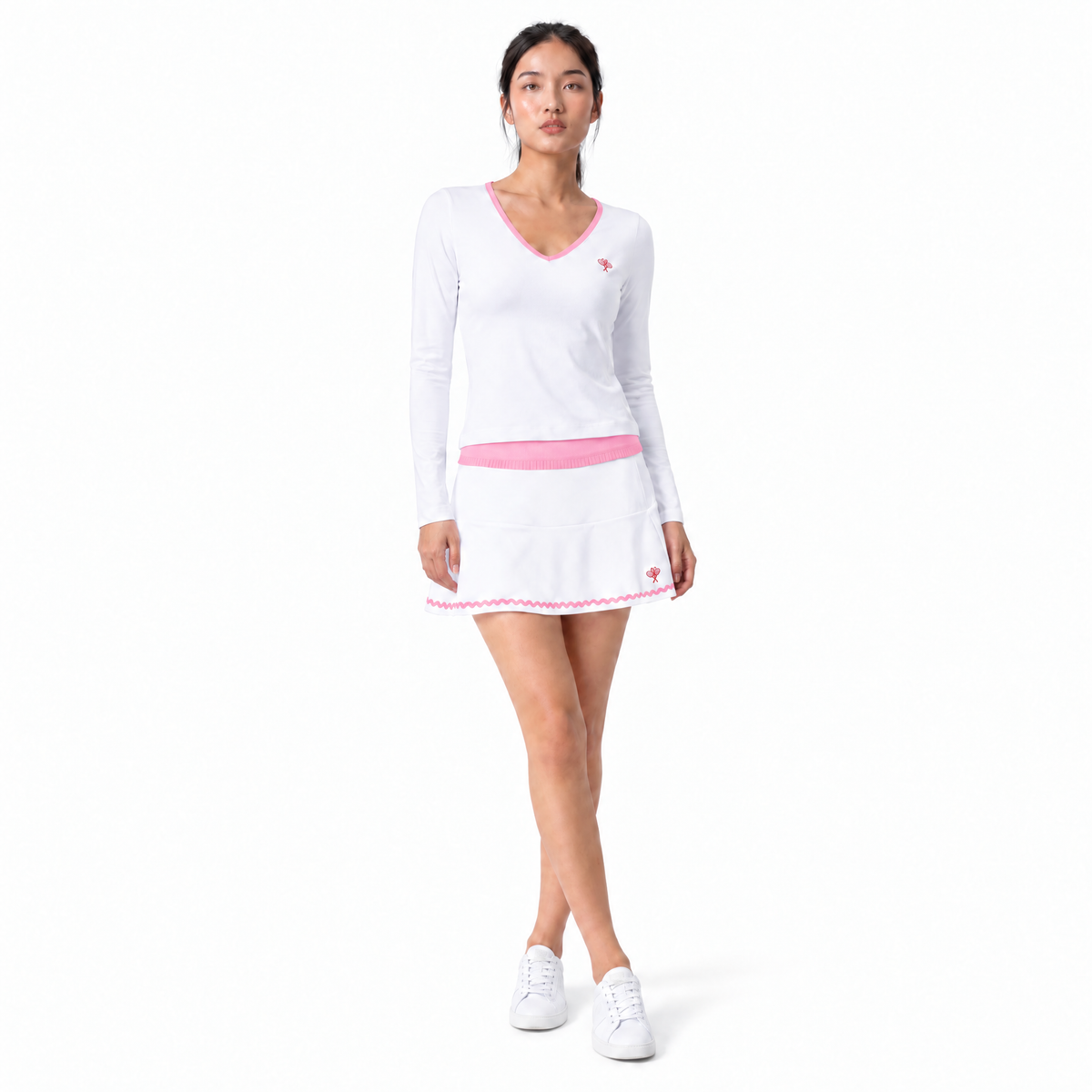 Woman wearing white tennis outfit with pink detailing and white sneakers on flat white background