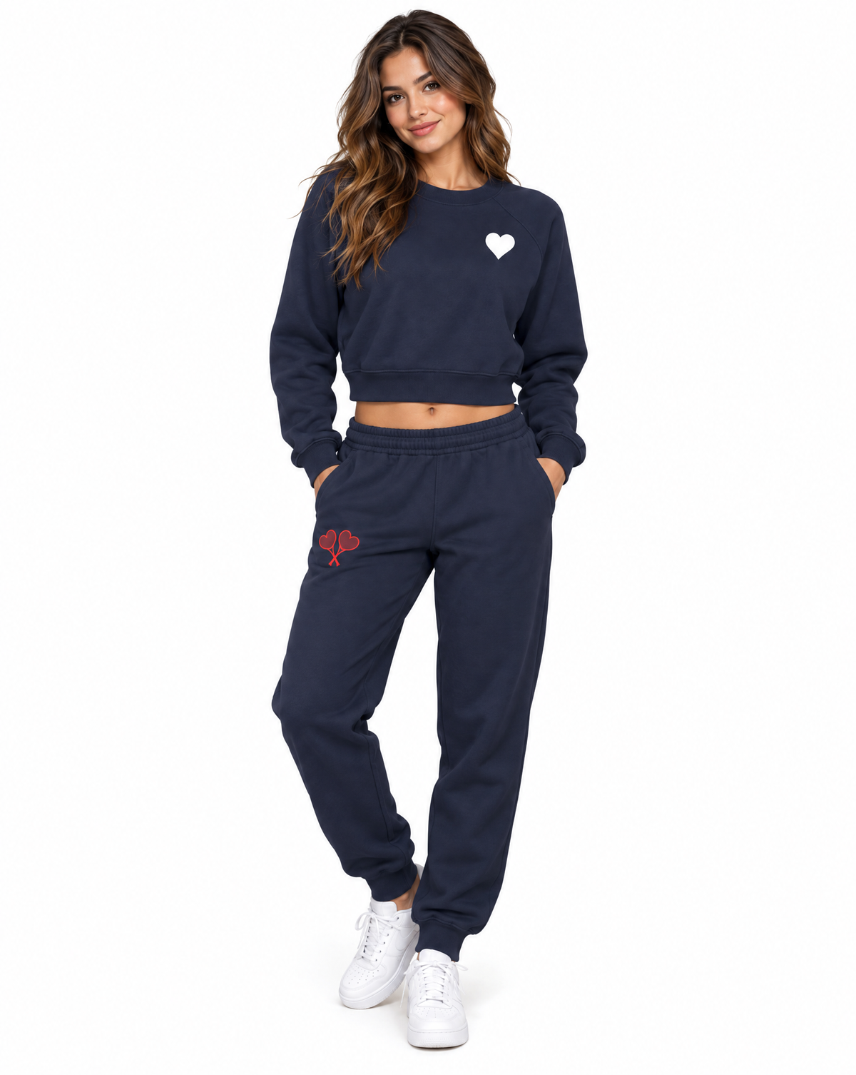 A woman modeling a navy blue sweatshirt and sweatpants set. The sweatshirt features a small white heart on the left chest, and the matching sweatpants have a small red heart on the left thigh.