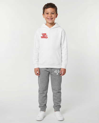 Boy wearing a white sweatshirt with red logo and white sweatpants with white logo on grey studio background