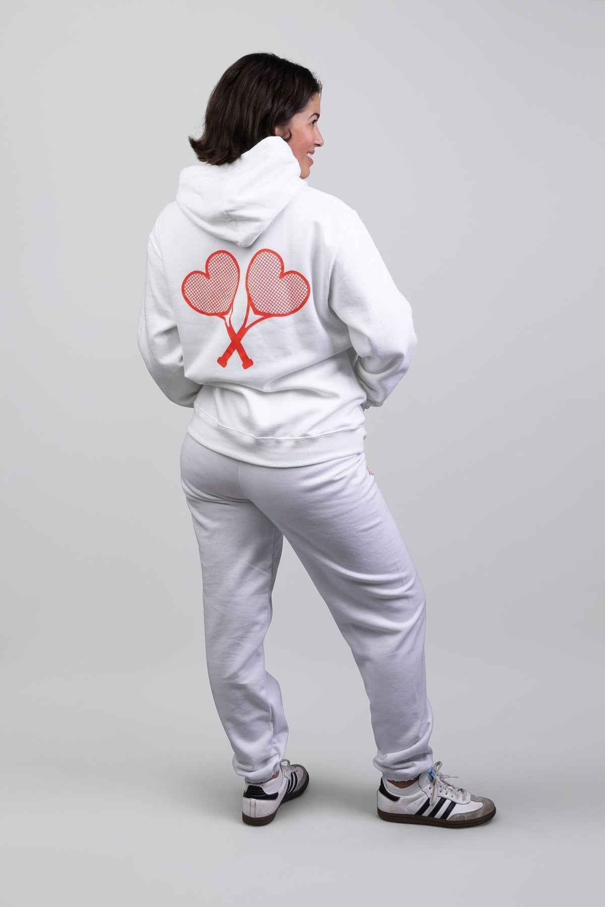 Person wearing a white hoodie with a red heart design on the back, standing against a plain background.