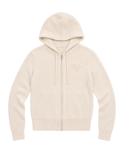 A cream-colored zip-up hoodie with a drawstring hood, kangaroo pockets, and a small tonal embroidered logo on the left chest, displayed against a solid white background.
