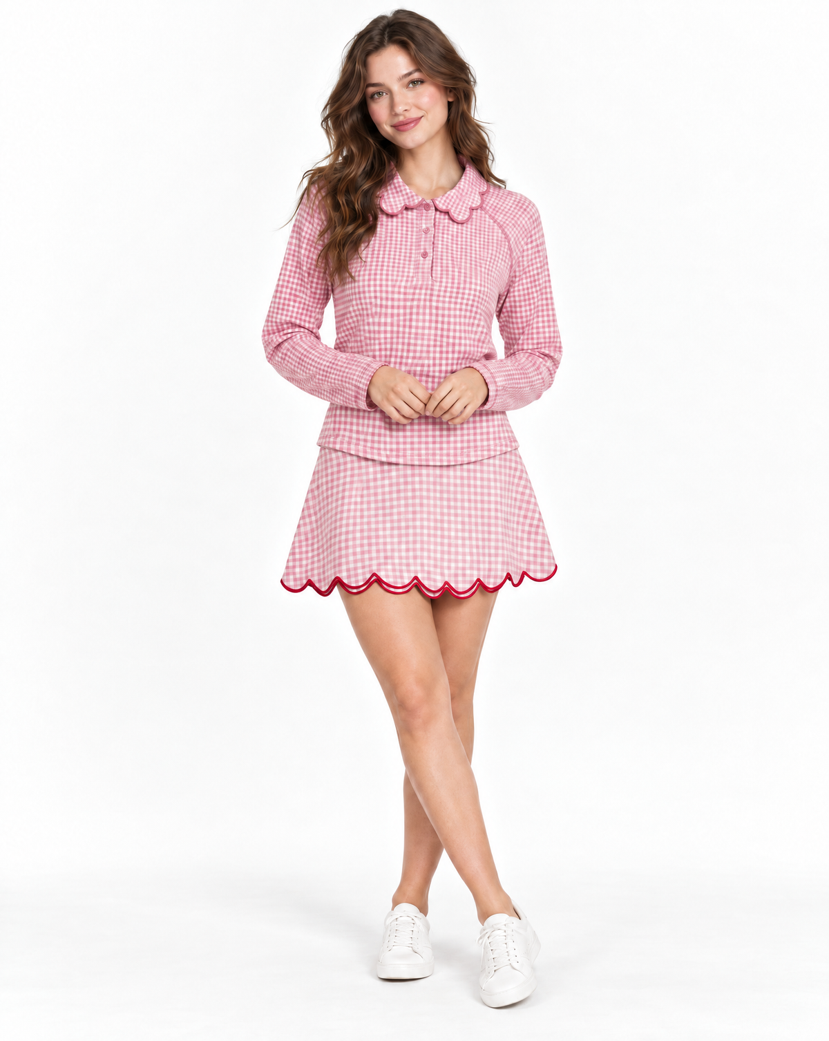 A woman modeling a pink and white gingham long-sleevetop with a scalloped Peter Pan collar and skirt with scalloped hem, paired with white sneakers, against a plain white studio background.