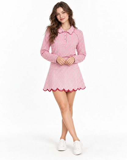 A woman modeling a pink and white gingham long-sleeve skirt and top with a scalloped Peter Pan collar and hem, paired with white sneakers, against a plain white studio background.