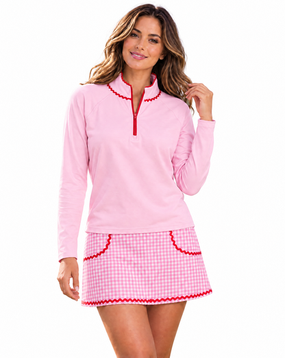 A woman modeling a light pink long-sleeve quarter-zip top and matching pink-and-white gingham mini skirt with red trim details, set against a plain white background.