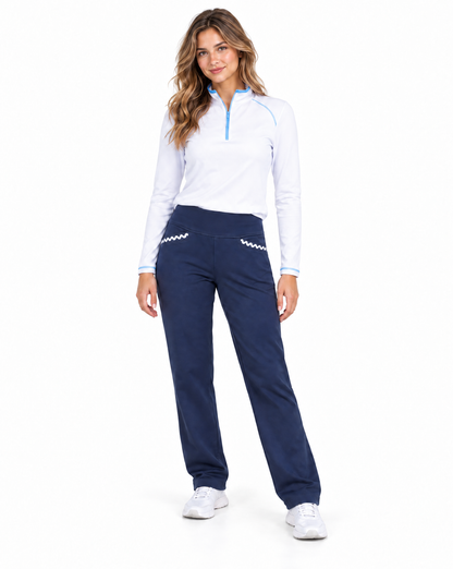 A woman modeling a white long-sleeve quarter-zip athletic top with light blue trim and navy blue athletic pants with white zigzag details, paired with white sneakers, on a solid white background.