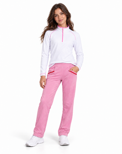 A woman modeling a white long-sleeve quarter-zip athletic top with pink trim and matching pink pants with red trim, standing against a plain white background.