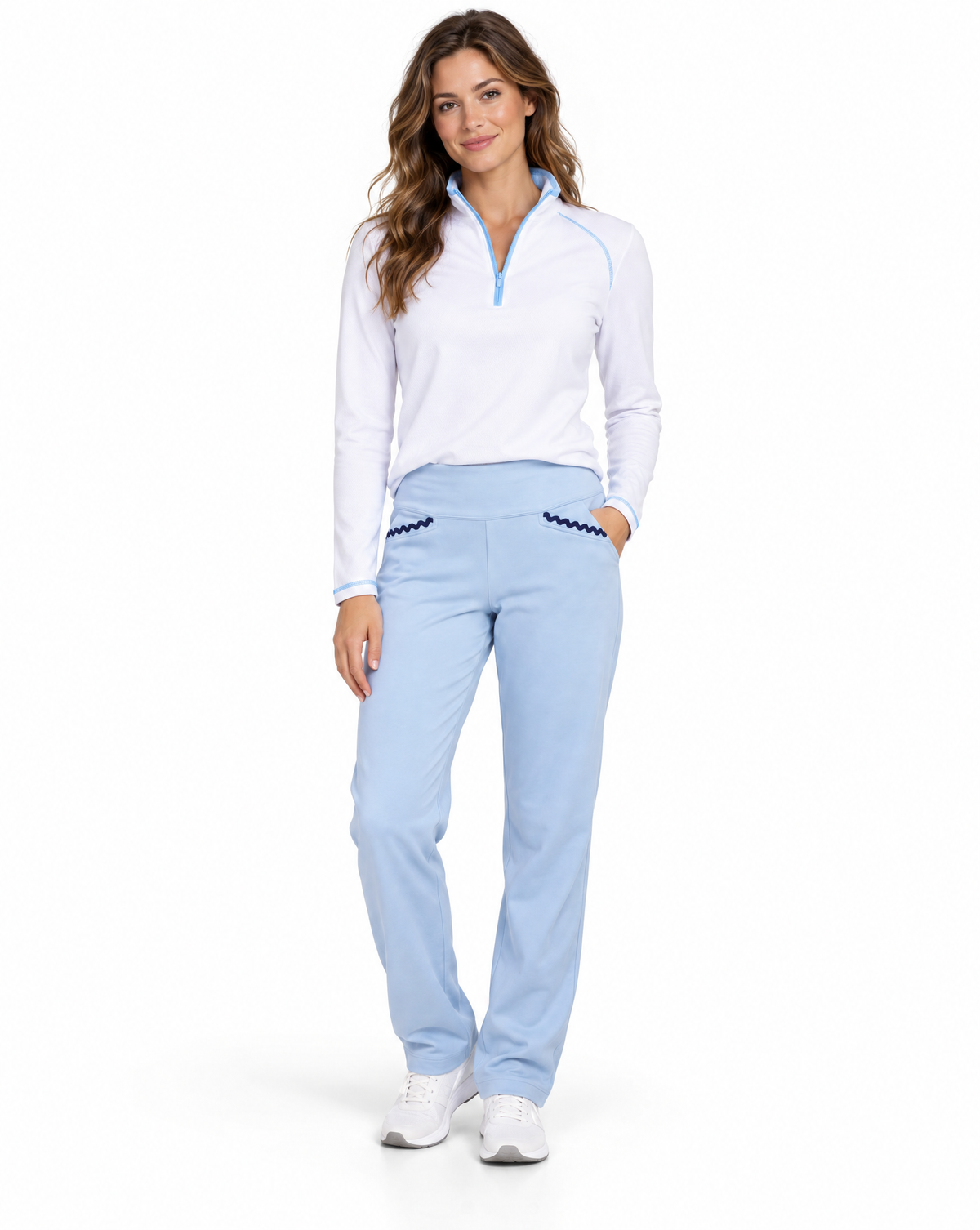 A woman modeling a white long-sleeve quarter-zip pullover with light blue trim and light blue pants with dark blue decorative stitching, paired with white sneakers, on a solid white background.