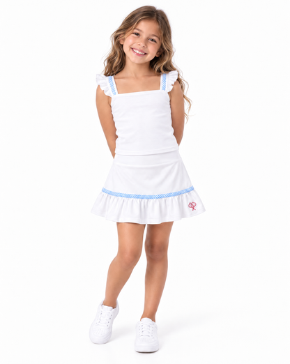 A young girl with long brown hair stands against a white background wearing a white sleeveless top and skirt with light blue trim and white sneakers.
