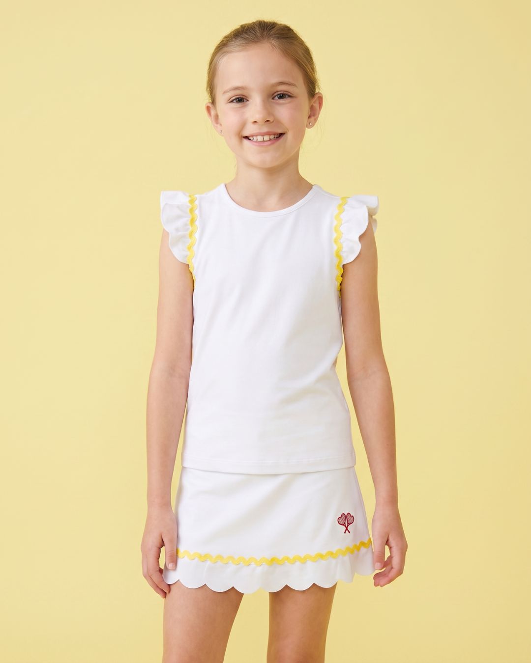 Young girl wearing a white dress with yellow trim on a yellow background
