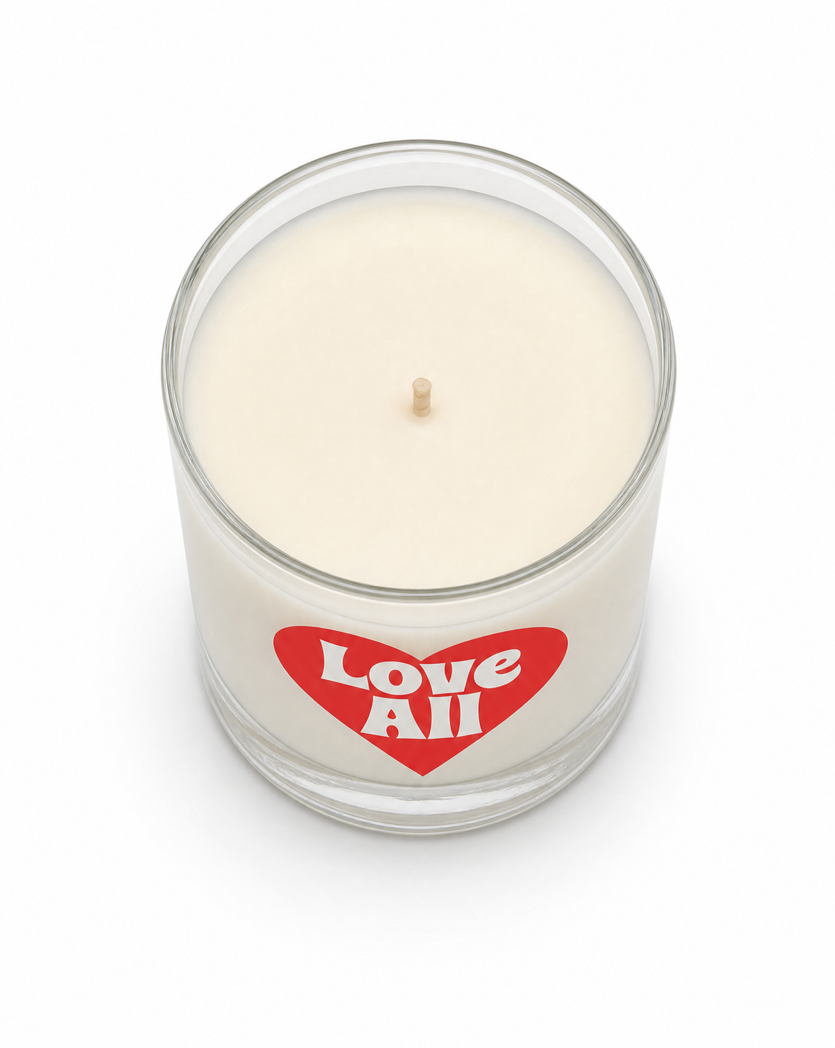 An off-white wax candle in a clear glass jar with a red heart-shaped label that reads 'Love All' in white text, set against a plain white background.