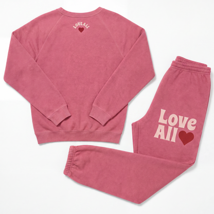 A two-piece matching loungewear set consisting of a long-sleeve sweatshirt and sweatpants in a dusty rose pink color. The sweatshirt features the text 'LOVE ALL' in a light pink arched font above a dark red heart on the upper back.
