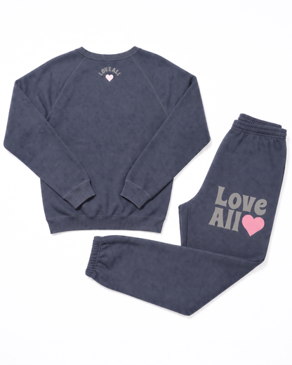 A two-piece lounge set consisting of a crewneck sweatshirt and matching joggers in a washed grey color. The sweatshirt features a small white heart and text on the back, while the joggers feature 'Love All' in white text and a pink heart on the left thigh