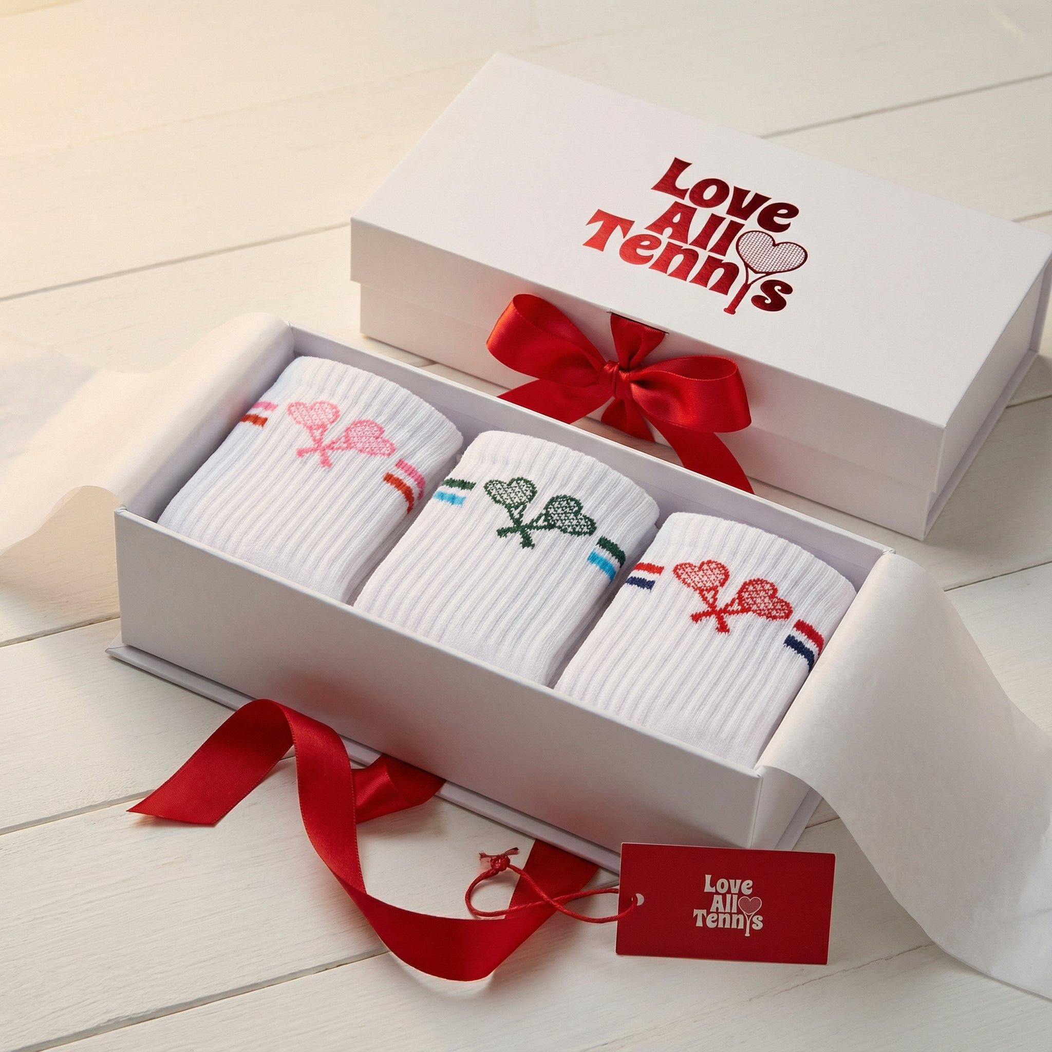 Three pairs of socks in a gift box with a red ribbon on a light wooden surface.