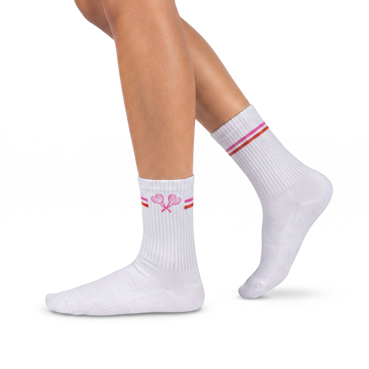 A pair of white ribbed crew socks worn on a model's feet, featuring a pink tennis racket graphic and thin pink and orange stripes near the cuff, set against a plain white background.