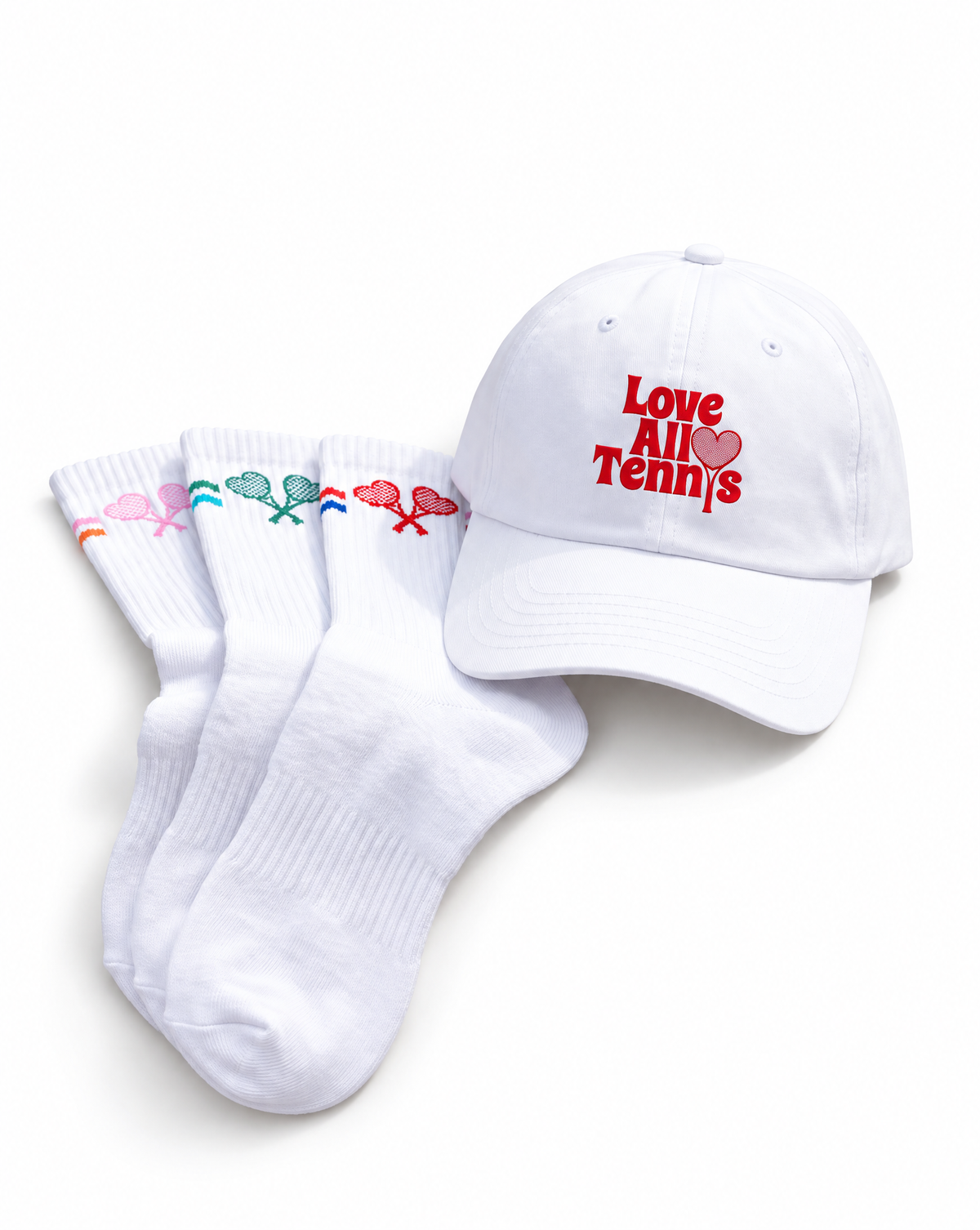 A white baseball cap with red embroidered text reading 'Love All Tennis' and a small red heart, shown next to three white crew socks with colorful tennis rackets embroidered near the cuffs.