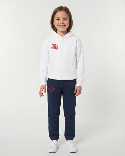 Child wearing a white hoodie and navy tracksuit with red designs on a white background
