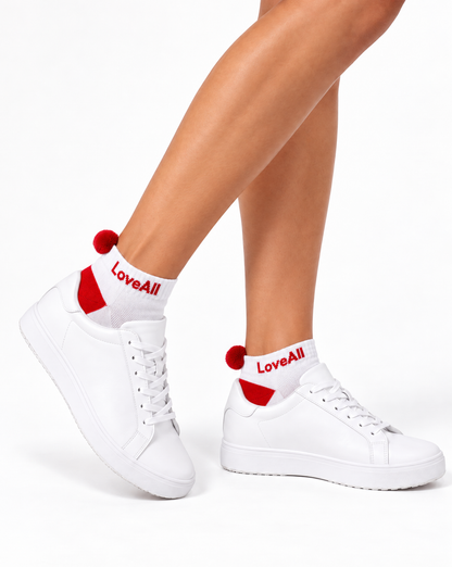 White low-top sneakers with white crew socks featuring red heel accents, red pom-poms, and the brand name 'LoveAll' printed in red on the socks, shown on a model's feet against a white background.