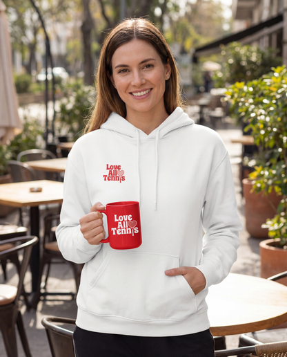 A person in a white sweatshirt holding a bright red ceramic mug, set against a sidewalk of tables