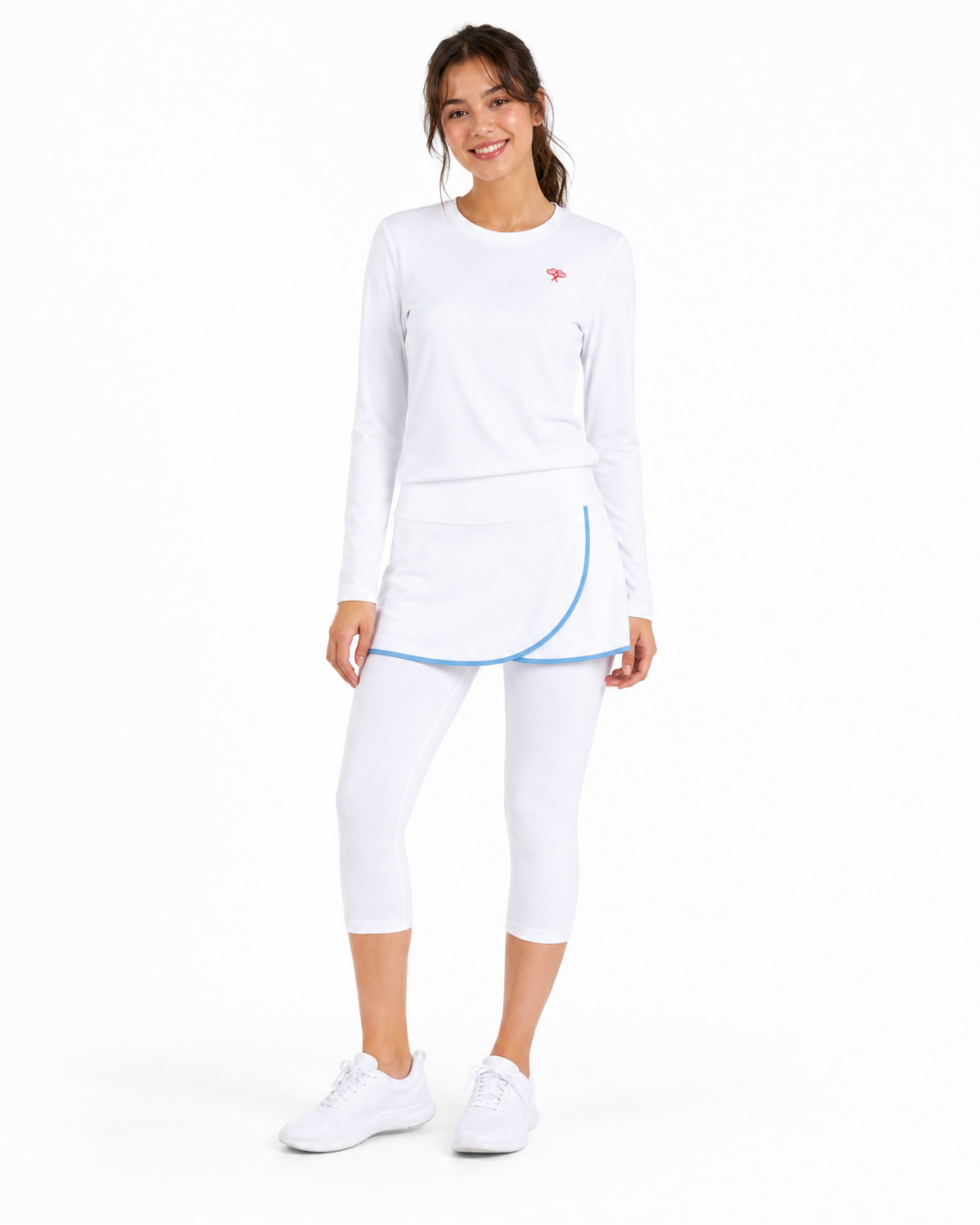 A woman modeling a white long-sleeve athletic top and matching white capri leggings with a light blue curved trim detail, paired with white sneakers, against a plain white background.