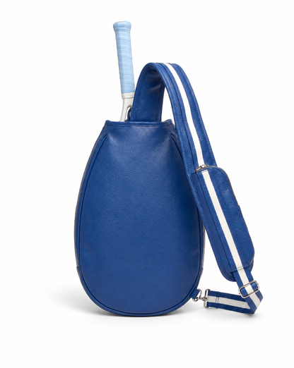 A royal blue leather tennis bag with a matching shoulder strap featuring white stripes, shown with a tennis racket tucked inside on a white background.