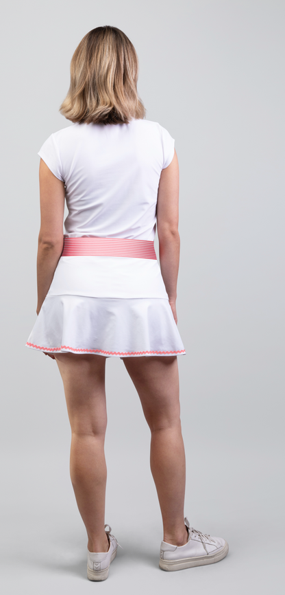 Woman wearing a white tennis outfit with a pink waistband on a gray background