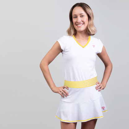 Woman wearing a white tennis dress with yellow accents on a gray background