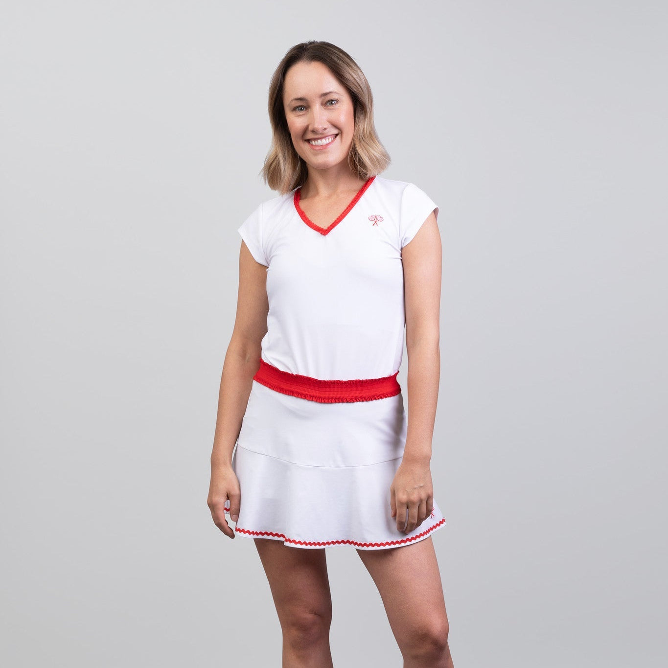 Woman wearing a white tennis skort and top with red accents on a gray background