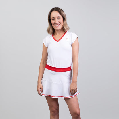 Woman wearing a white tennis skort and top with red accents on a gray background