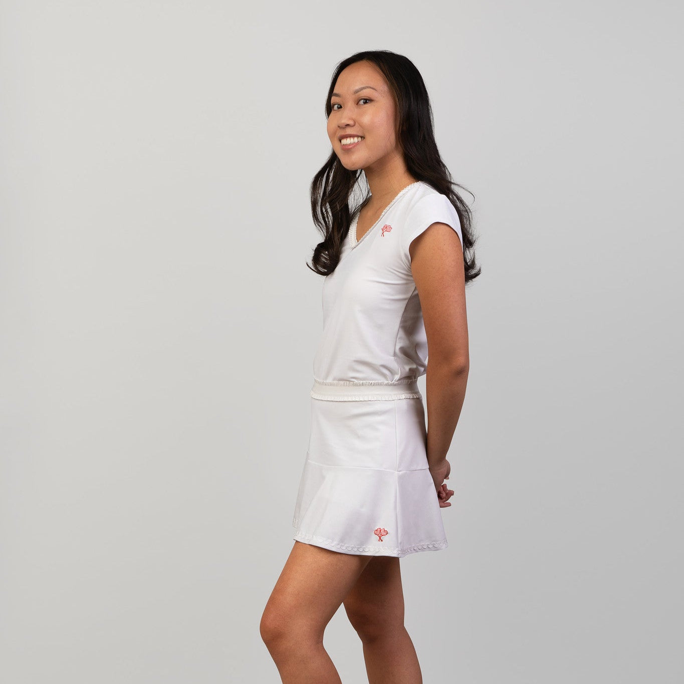 Woman wearing a white top and skort with a logo on a gray background
