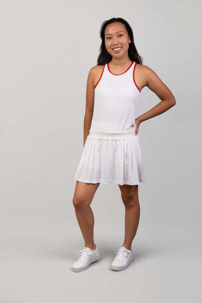 Woman wearing a white tennis outfit with red accents on a gray background