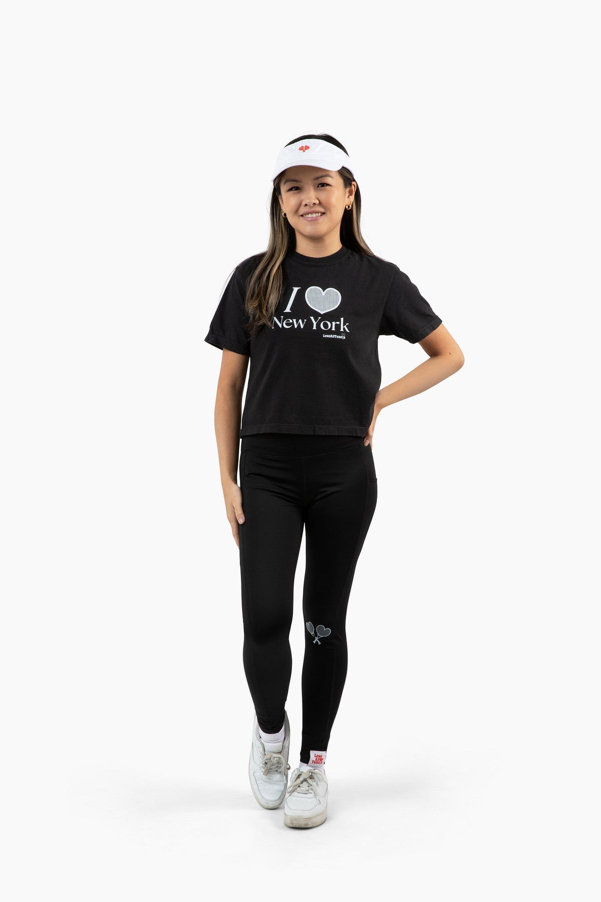 Person wearing a black 'I ❤️ New York' t-shirt, black leggings, and white sneakers on a white background